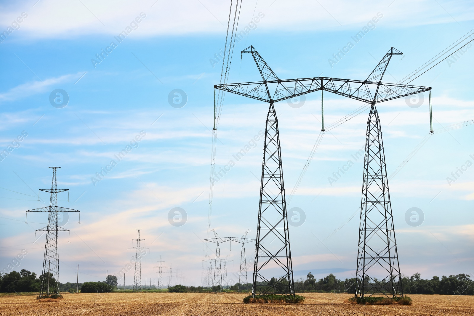 Photo of High voltage towers with electricity transmission power lines in field on sunny day