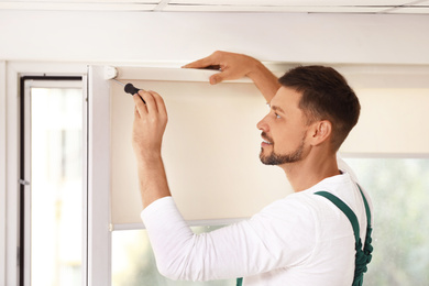Image of Handyman with screwdriver installing roller window blind indoors
