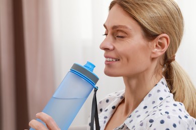 Photo of Happy woman with bottle of water in room
