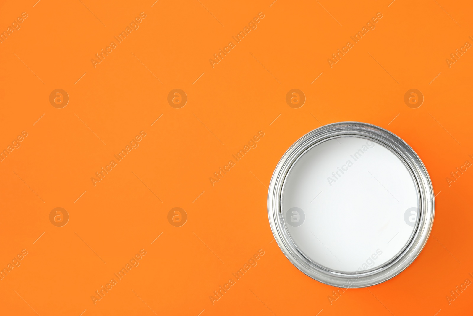 Photo of Open can of white paint on orange background, top view. Space for text