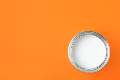 Open can of white paint on orange background, top view. Space for text