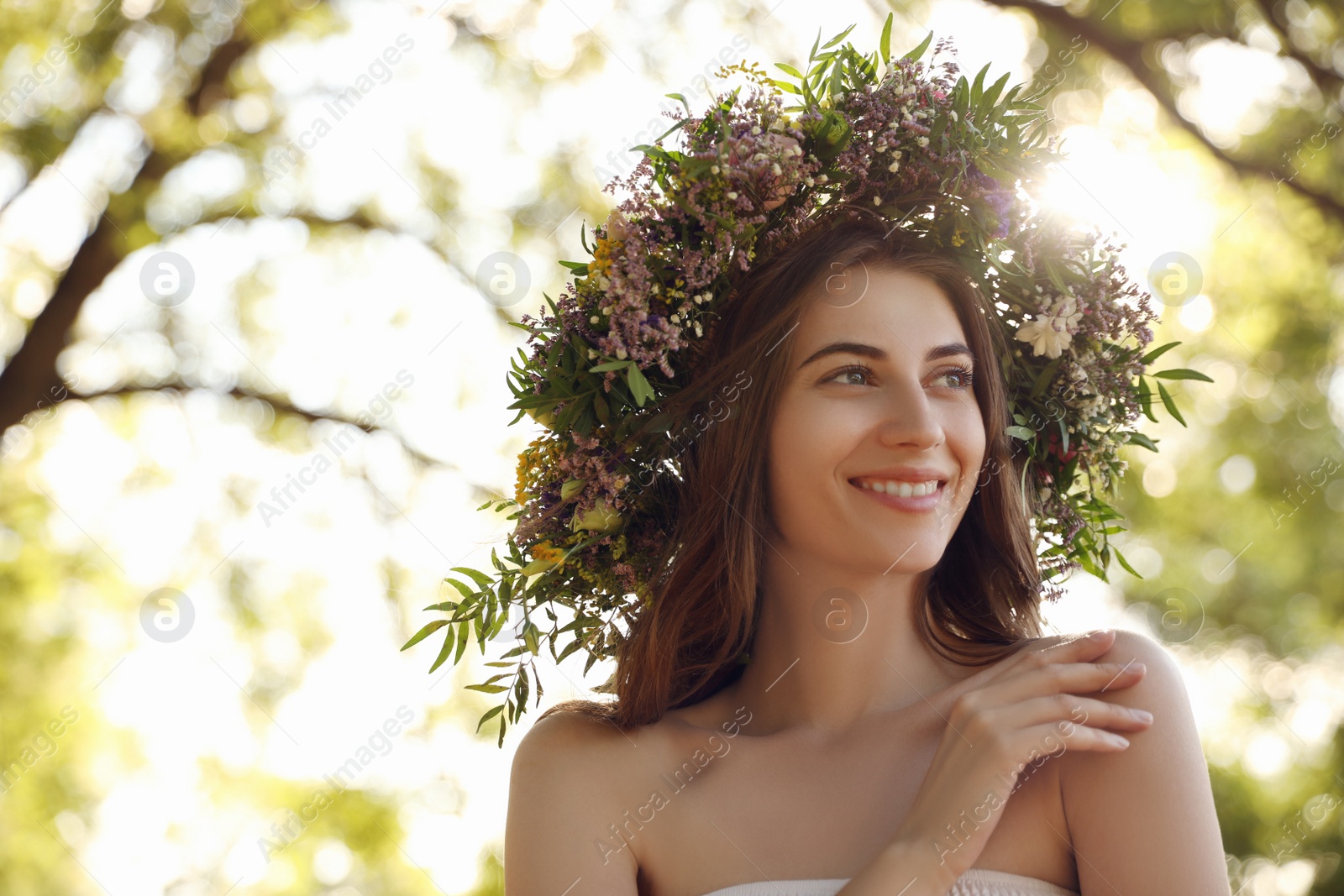 Photo of Young woman wearing wreath made of beautiful flowers outdoors on sunny day