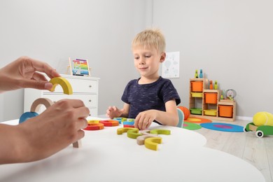 Photo of Motor skills development. Mother helping her son to play with colorful wooden arcs at white table in room