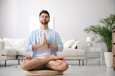 Photo of Young man meditating on straw cushion at home