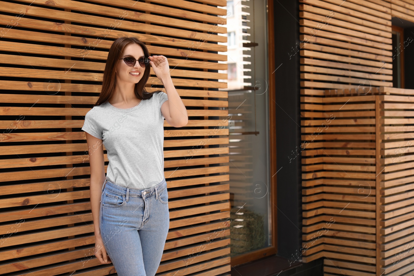 Photo of Young woman wearing gray t-shirt near wooden wall on street. Urban style