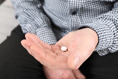 Senior man holding pill in hand, closeup