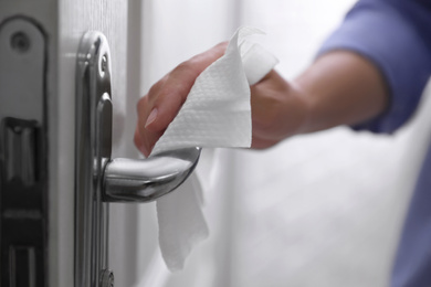 Photo of Woman cleaning door handle with wet wipe indoors, closeup