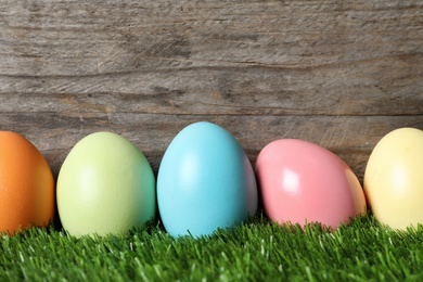 Photo of Colorful dyed Easter eggs on green grass against wooden background, space for text