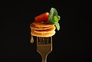 Photo of Fork with cereal pancakes, strawberry and mint on black background