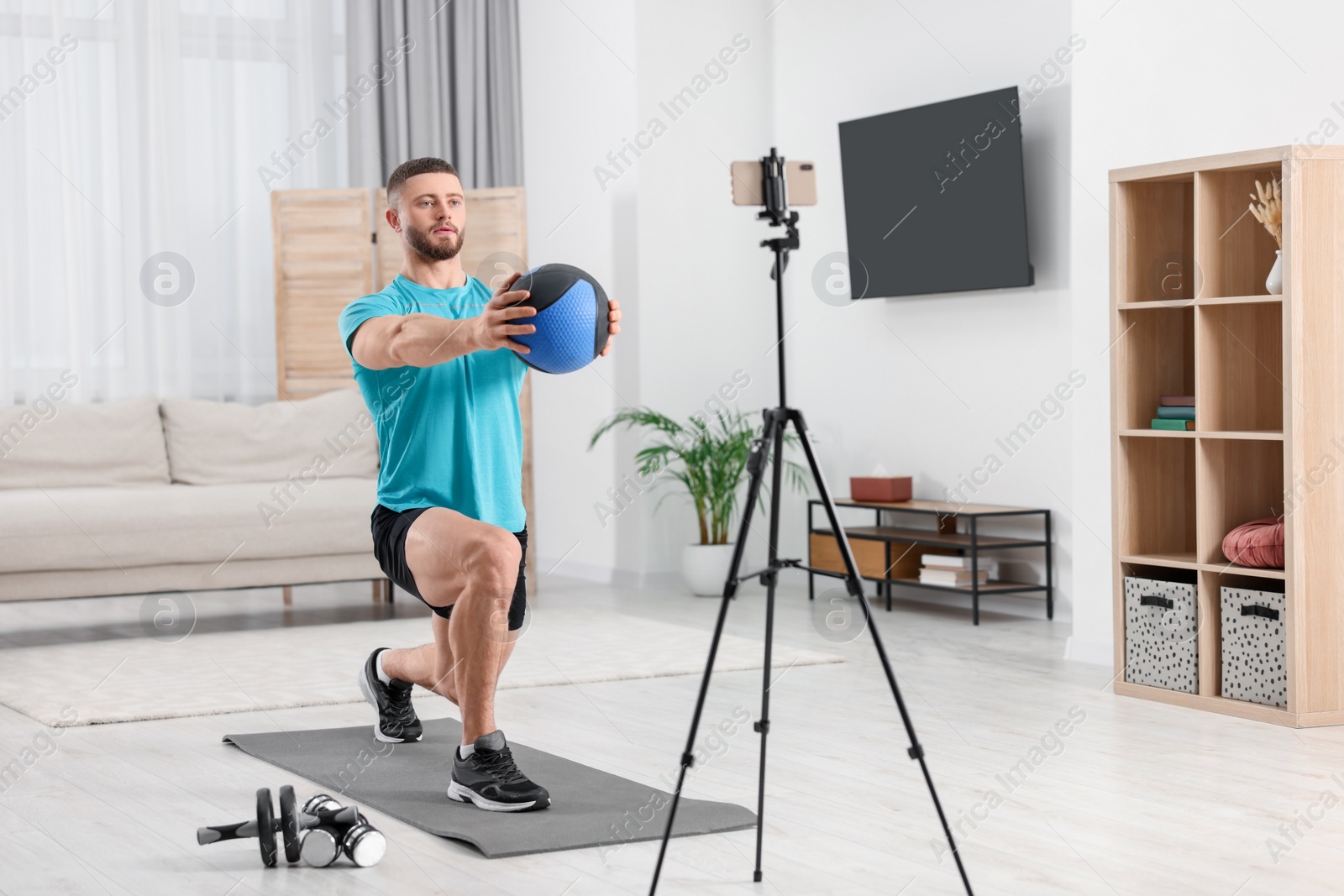 Photo of Trainer with ball streaming online workout on phone at home