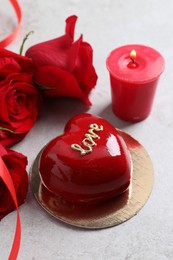 Photo of St. Valentine's Day. Delicious heart shaped cake, roses and candle on light table, closeup