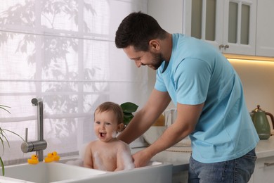 Father washing his little baby in sink at home