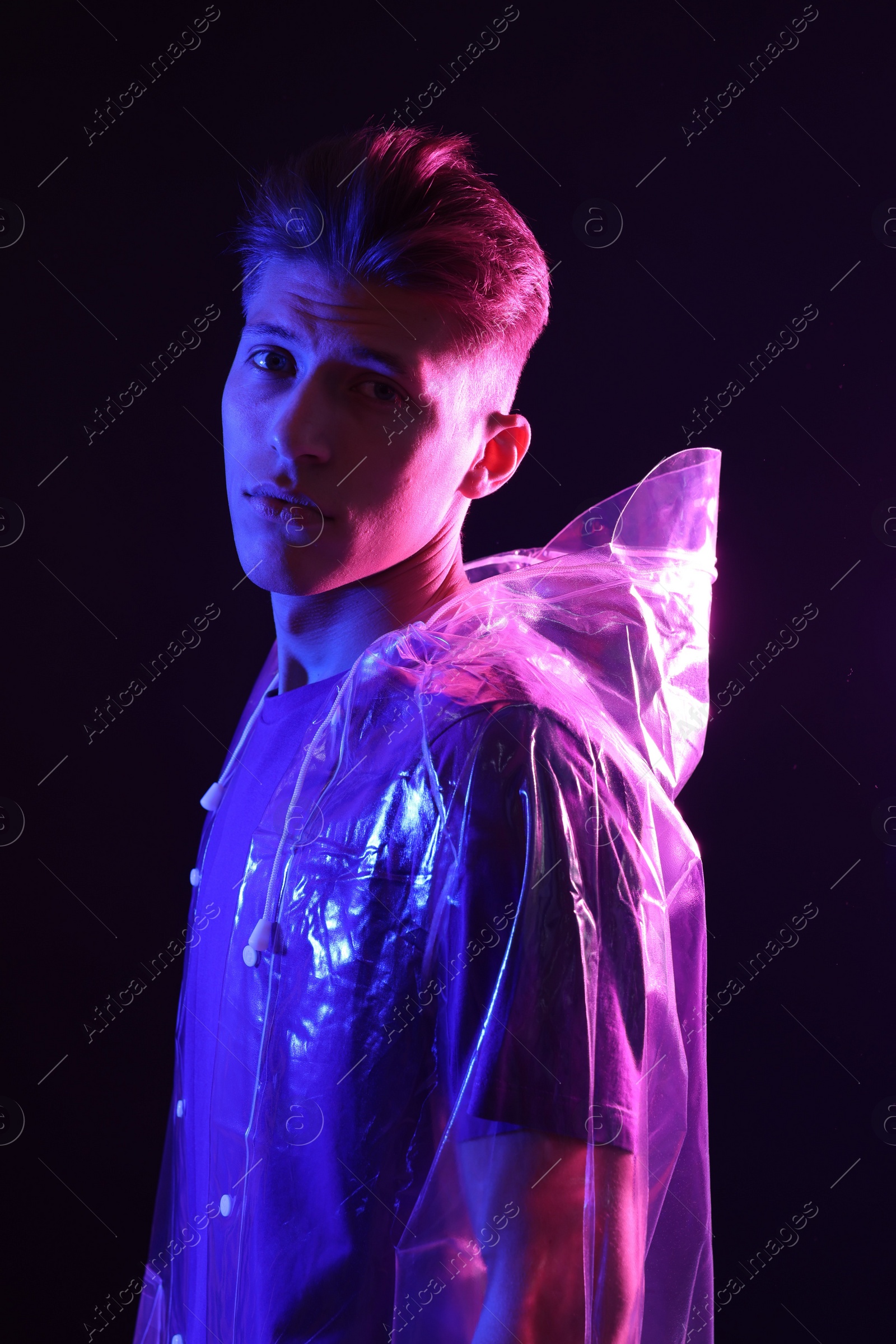 Photo of Young man wearing clear coat on dark background in neon lights