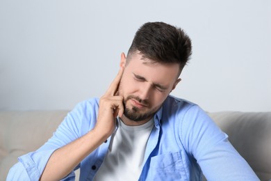 Young man suffering from ear pain at home