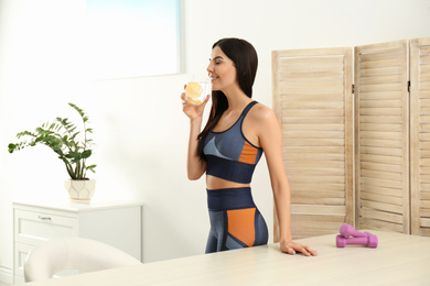 Photo of Beautiful sportive woman drinking fresh lemon water indoors