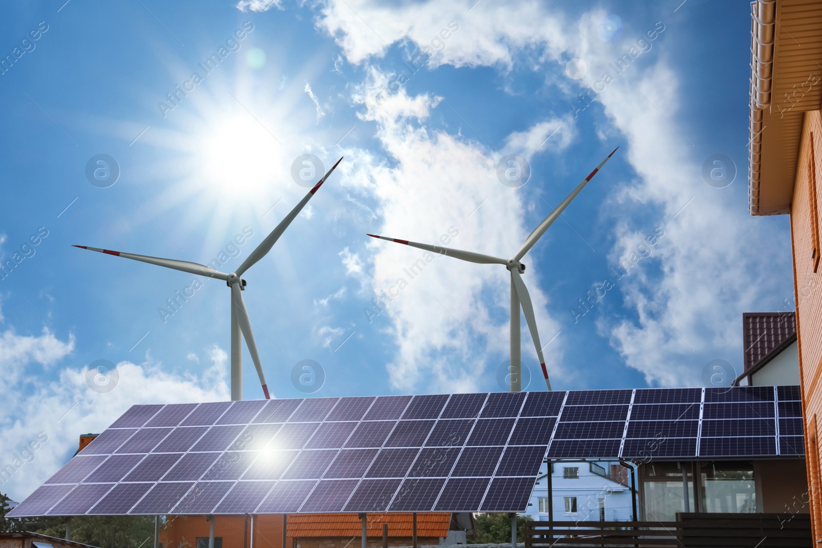 Image of Wind turbines near house with installed solar panels on roof. Alternative energy source