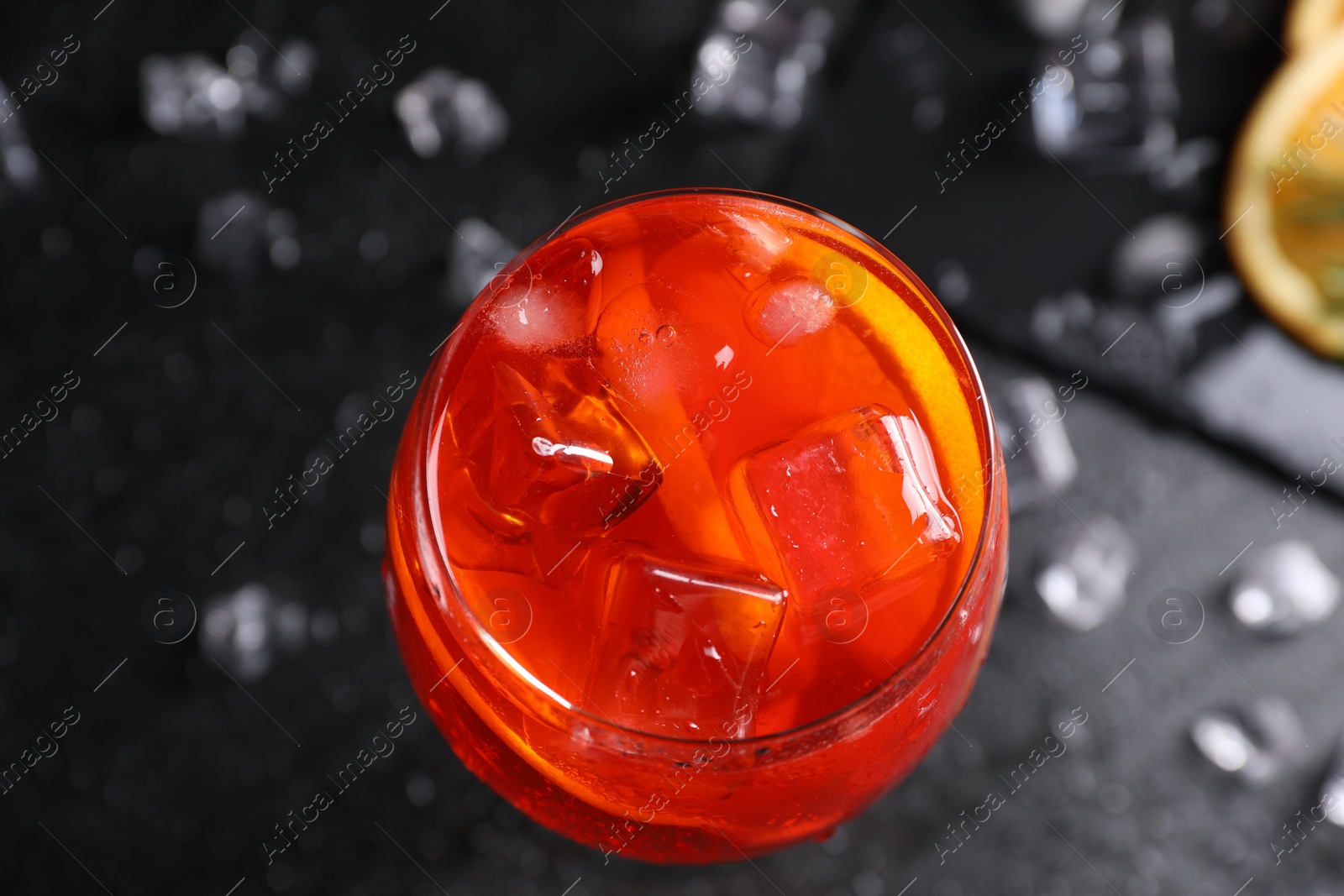 Photo of Glass of tasty Aperol spritz cocktail with ice cubes on dark gray table, top view