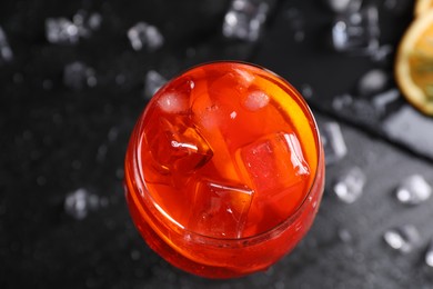 Photo of Glass of tasty Aperol spritz cocktail with ice cubes on dark gray table, top view
