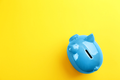 Photo of Blue piggy bank on yellow background, top view. Space for text