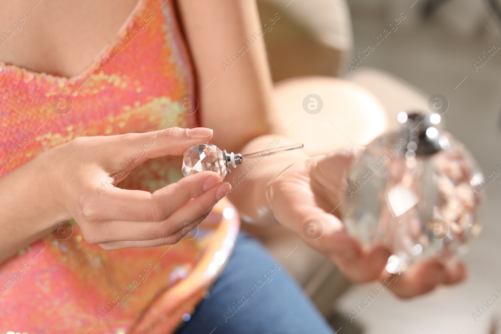 Photo of Young woman applying perfume on wrist against blurred background, closeup