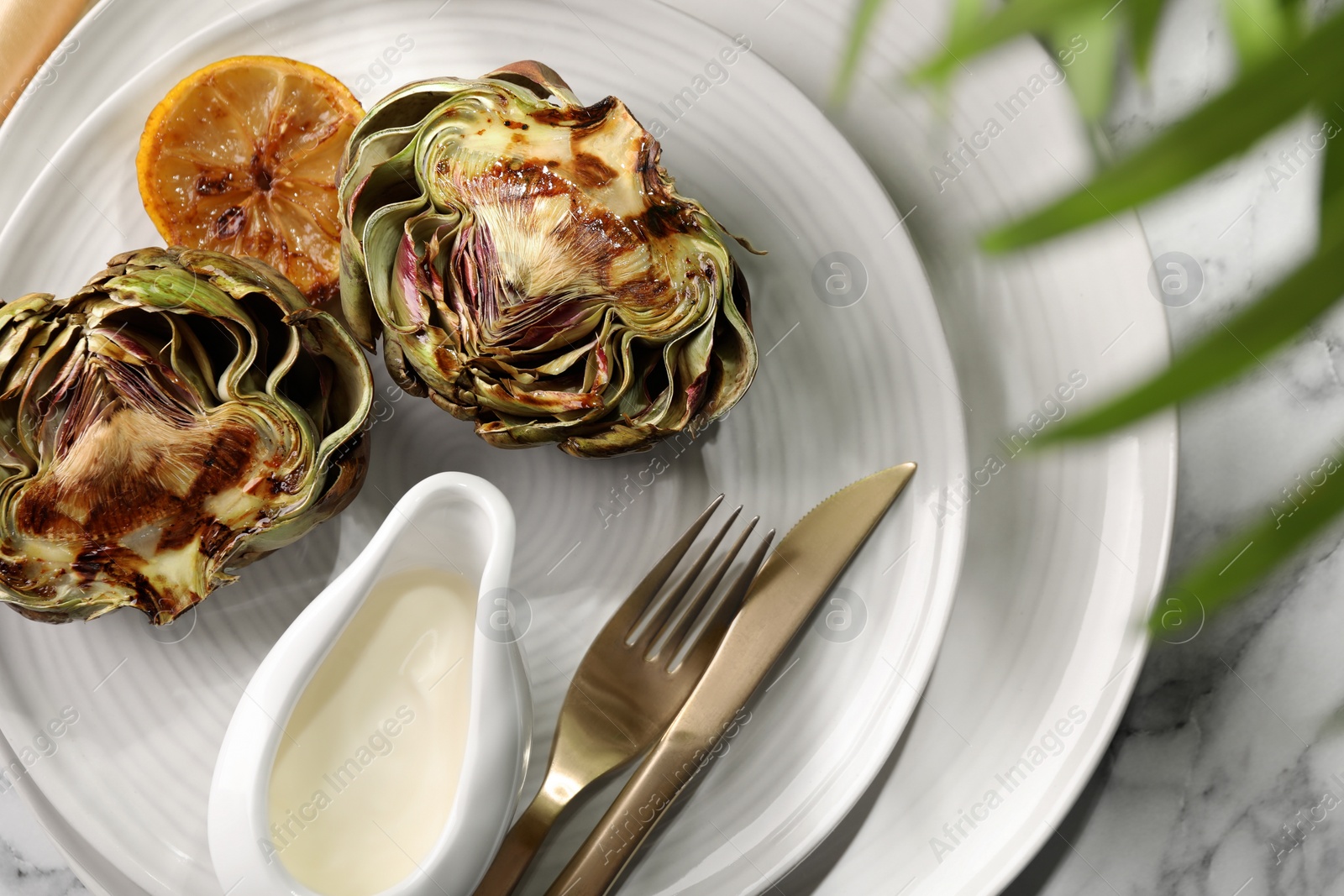 Photo of Tasty grilled artichokes served on white marble table, flat lay