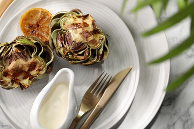 Tasty grilled artichokes served on white marble table, flat lay