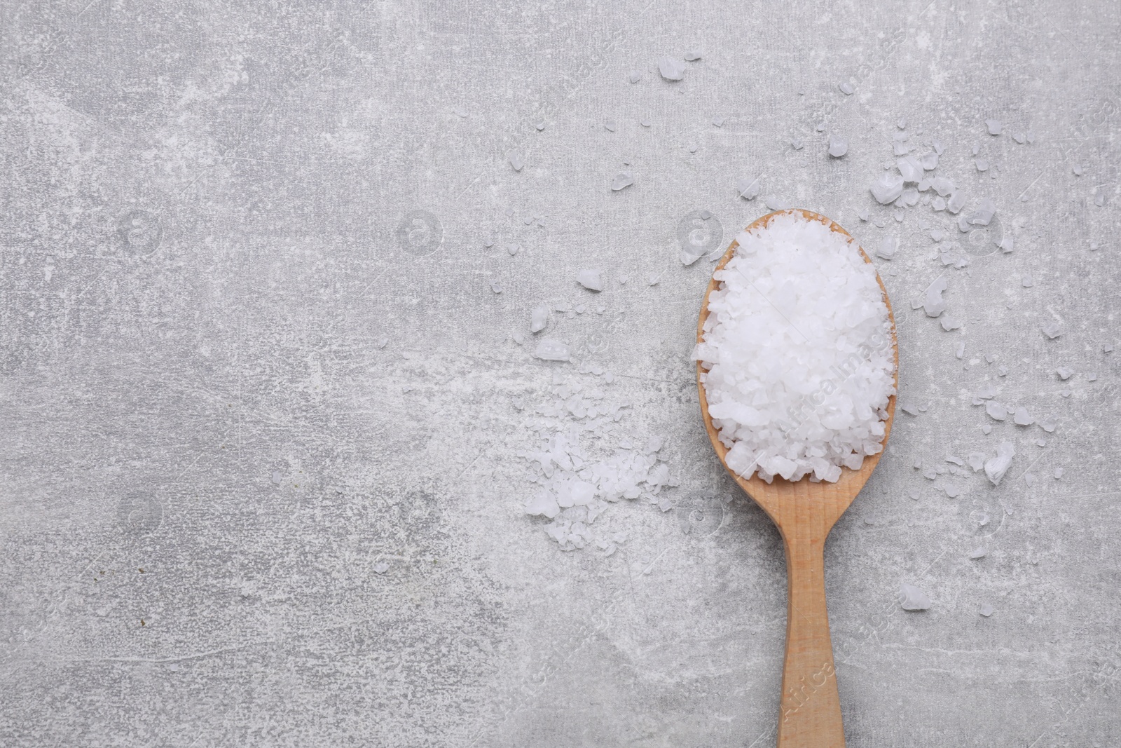 Photo of Spoon with sea salt on light grey table, top view. Space for text