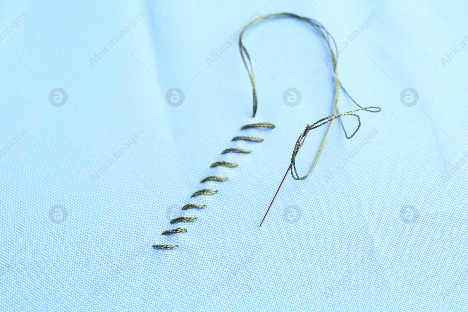 Photo of Sewing needle with thread and stitches on light blue cloth, closeup