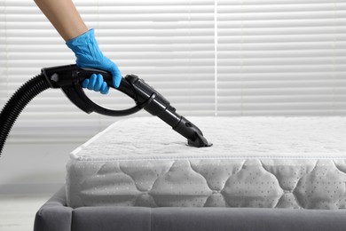 Woman disinfecting mattress with vacuum cleaner indoors, closeup. Space for text