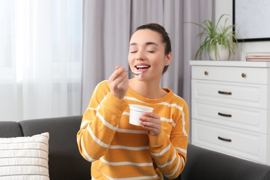 Happy woman eating tasty yogurt at home