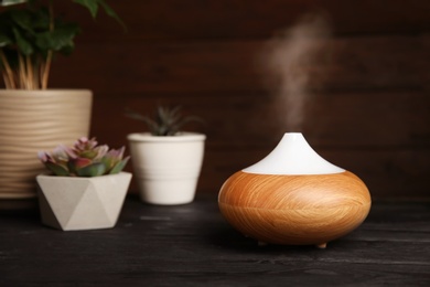 Photo of Composition with modern essential oil diffuser on black wooden table against dark background, space for text