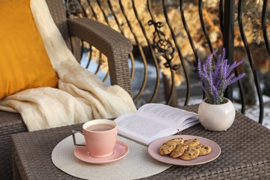 Photo of Cup with tasty cocoa, cookies and book on rattan table at balcony