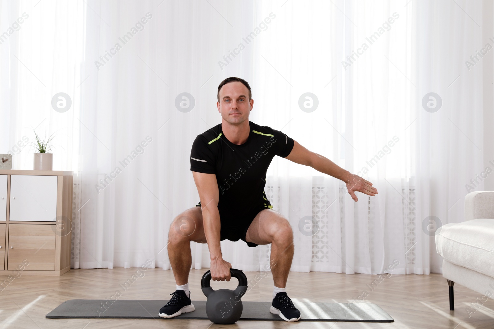 Photo of Muscular man training with kettlebell at home