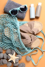 Photo of String bag and different beach accessories on pale orange background, flat lay