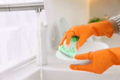 Woman washing plate above sink in modern kitchen, closeup. Space for text