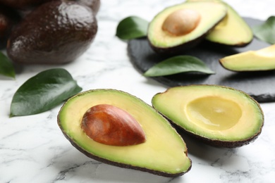 Whole and cut avocados with green leaves on white marble table, closeup