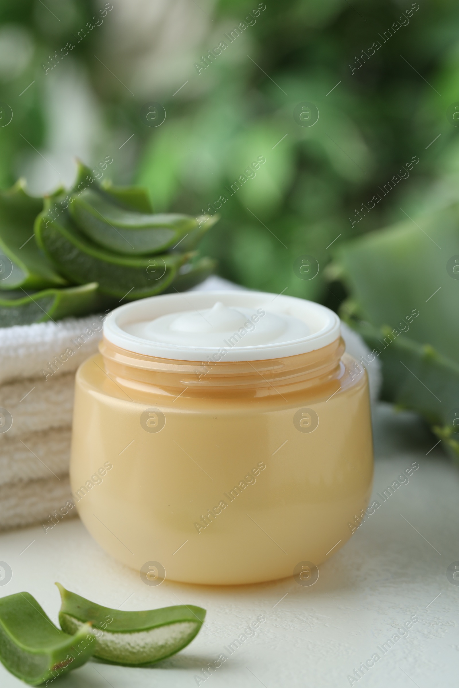 Photo of Jar with cream and cut aloe leaves on white table against blurred green background, closeup