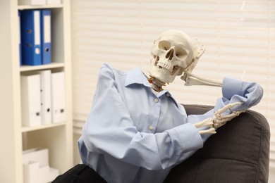 Waiting concept. Human skeleton sitting in armchair at office