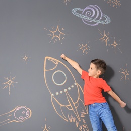 Photo of Cute little child playing with chalk rocket drawing on grey background