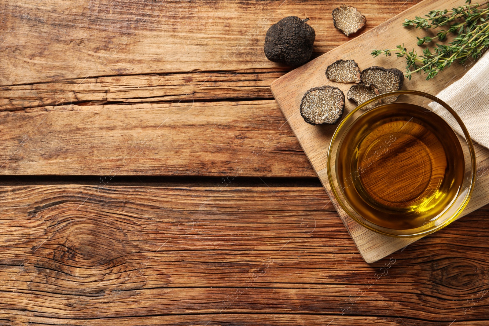 Photo of Fresh truffles, thyme and oil in glass bowl on wooden table, flat lay. Space for text