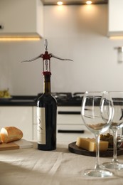 Wine bottle with corkscrew, wineglasses and food on table in kitchen