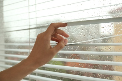 Woman opening window blinds, closeup. Space for text