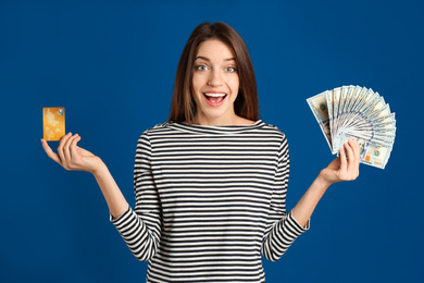 Photo of Excited young woman with cash money and credit card on blue background