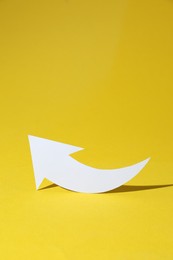 Photo of White curved paper arrow on yellow background, space for text