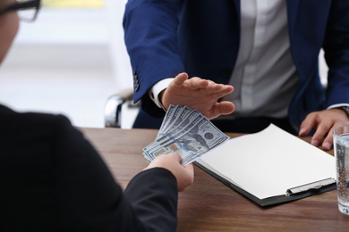 Businessman refuses to take bribe money at wooden table, closeup