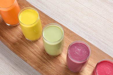 Board with many different tasty smoothies on white wooden table