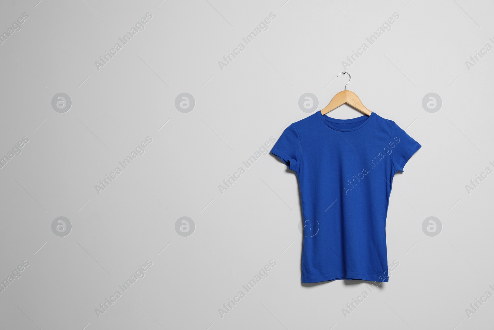 Photo of Hanger with blue t-shirt on light wall. Mockup for design