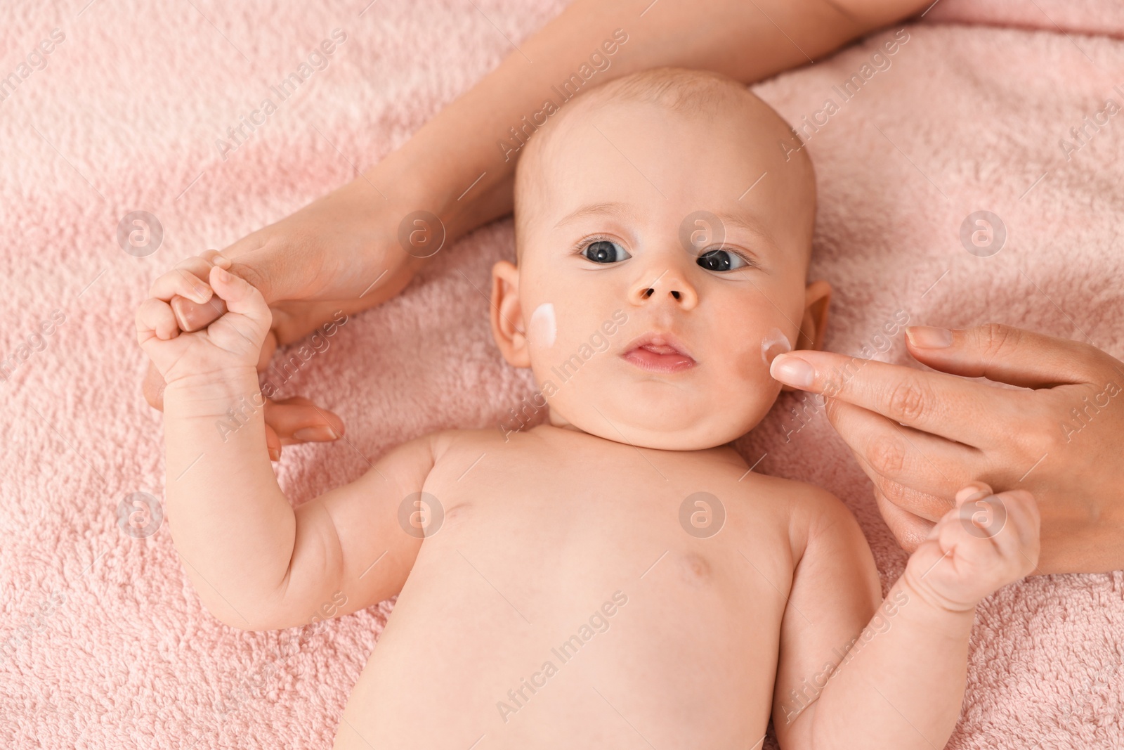 Photo of Woman applying cream onto baby`s face on bed, closeup