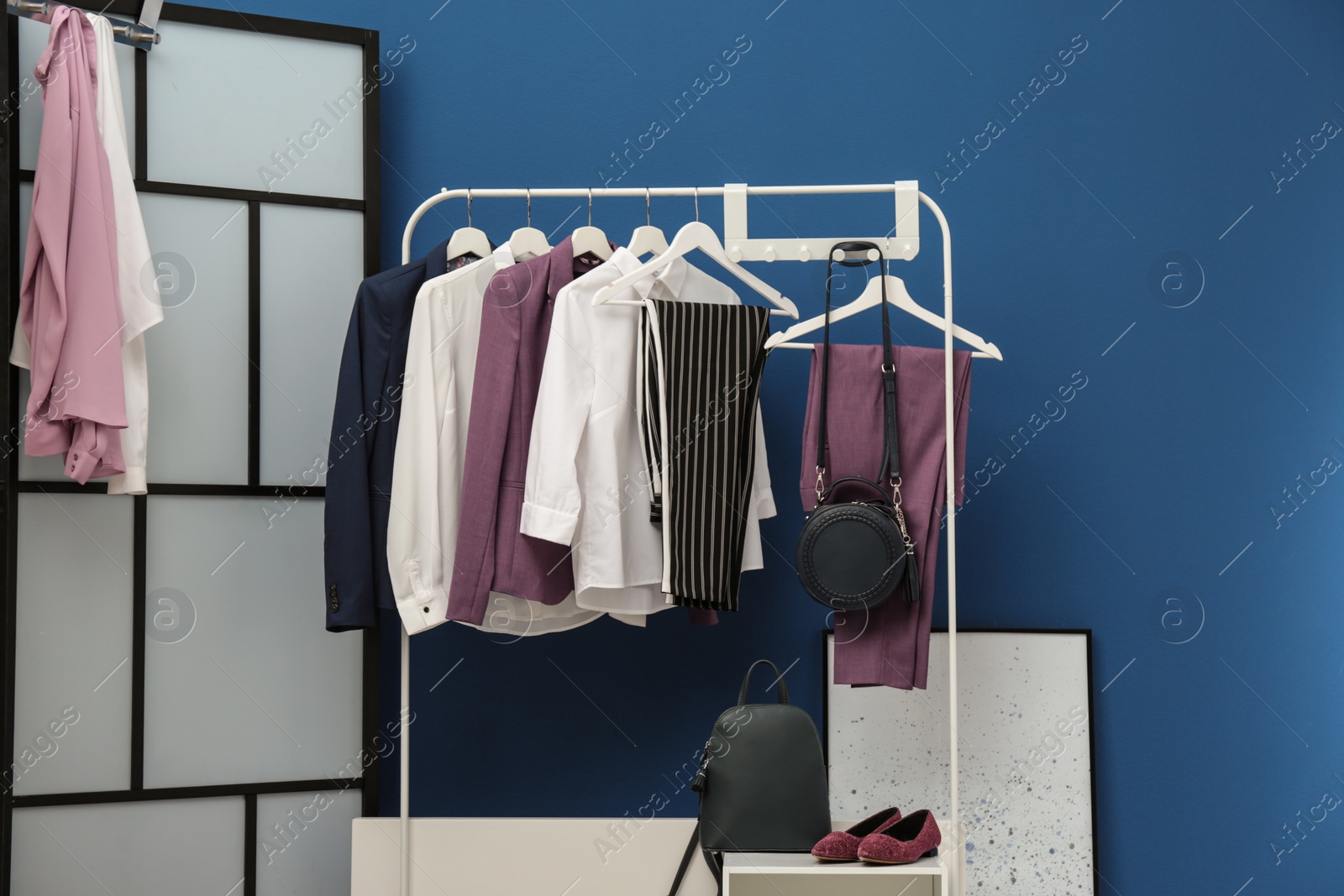 Photo of Wardrobe rack with women's clothes and shoes at blue wall in room