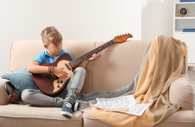 Cute little boy playing guitar on sofa in room. Space for text